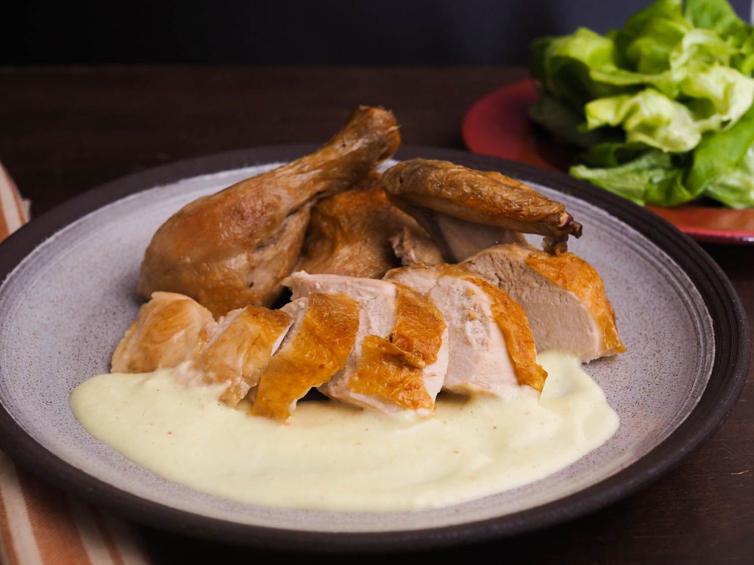 Sliced, roasted chicken on a ceramic plate with soubise sauce.
