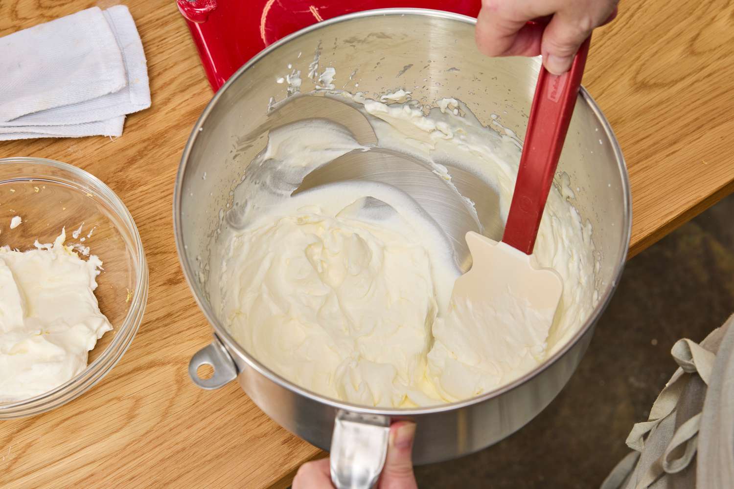 A person scooping whipped cream out of a stand mixer's bowl.