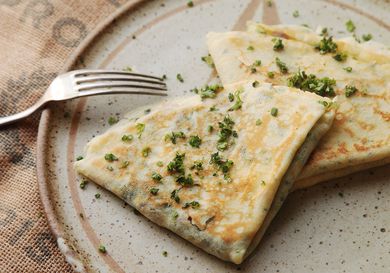 Two quarter-folded filled crepes garnished with chopped herbs on a plate