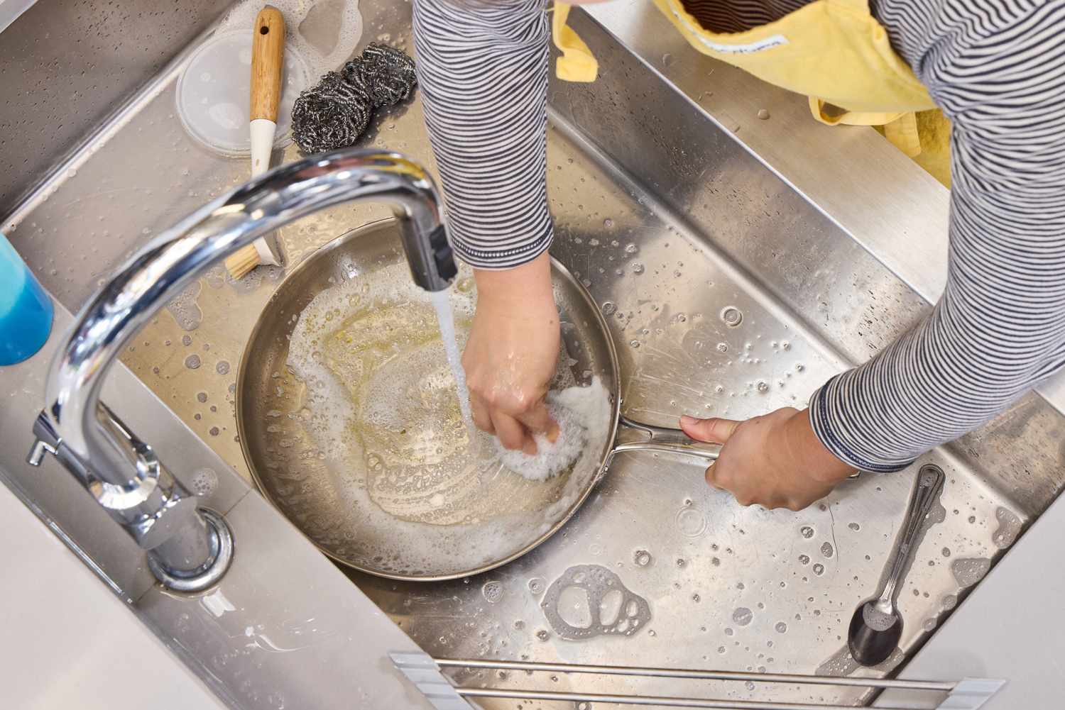 A person cleans the Tramontina 12-Inch Stainless Steel Skillet in a sink
