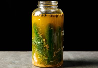 Open jar of homemade pickled cucumbers in brine, viewed from side.