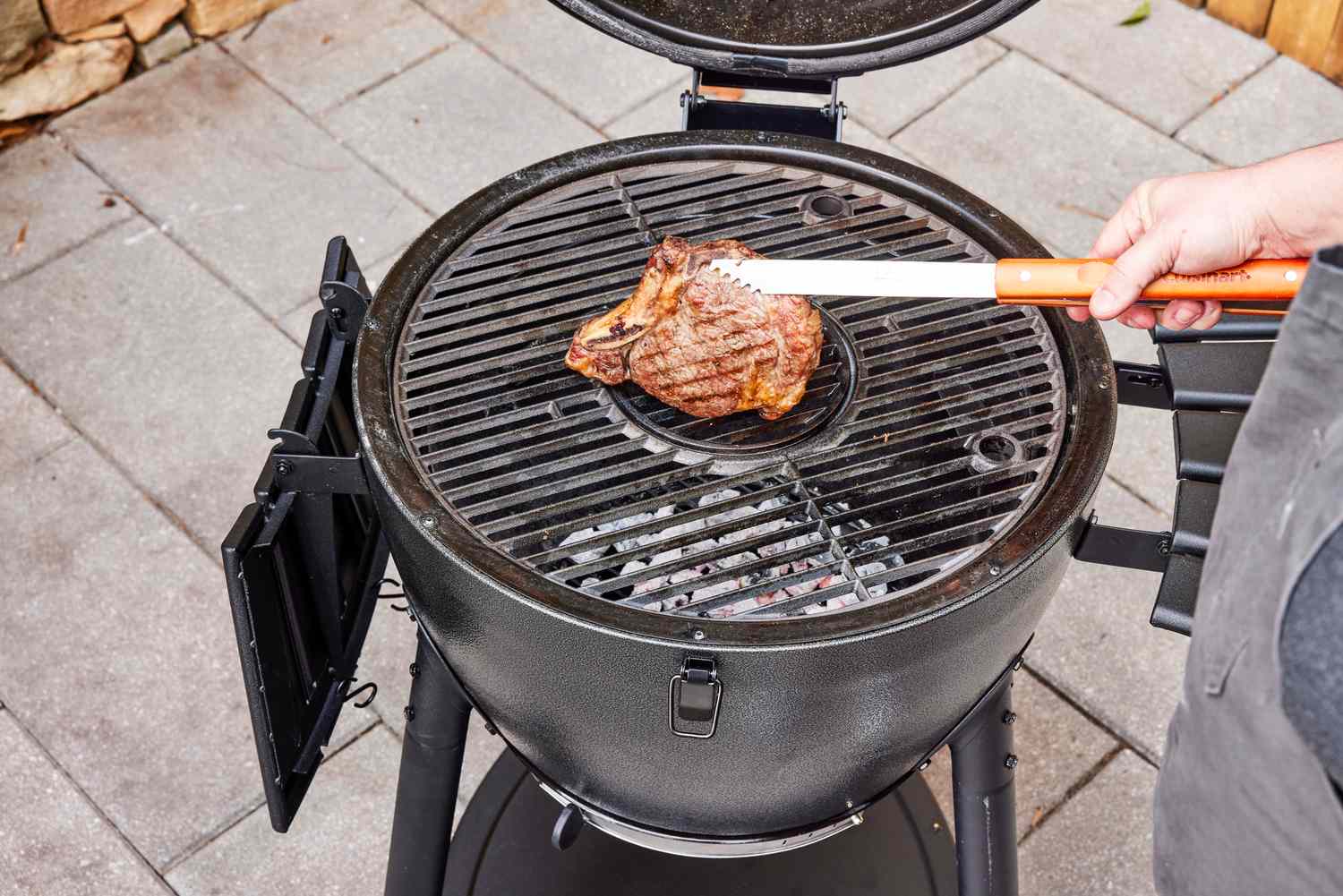 A person flips meat cooked in the Char-Griller E16620 Akorn Kamado Charcoal Grill