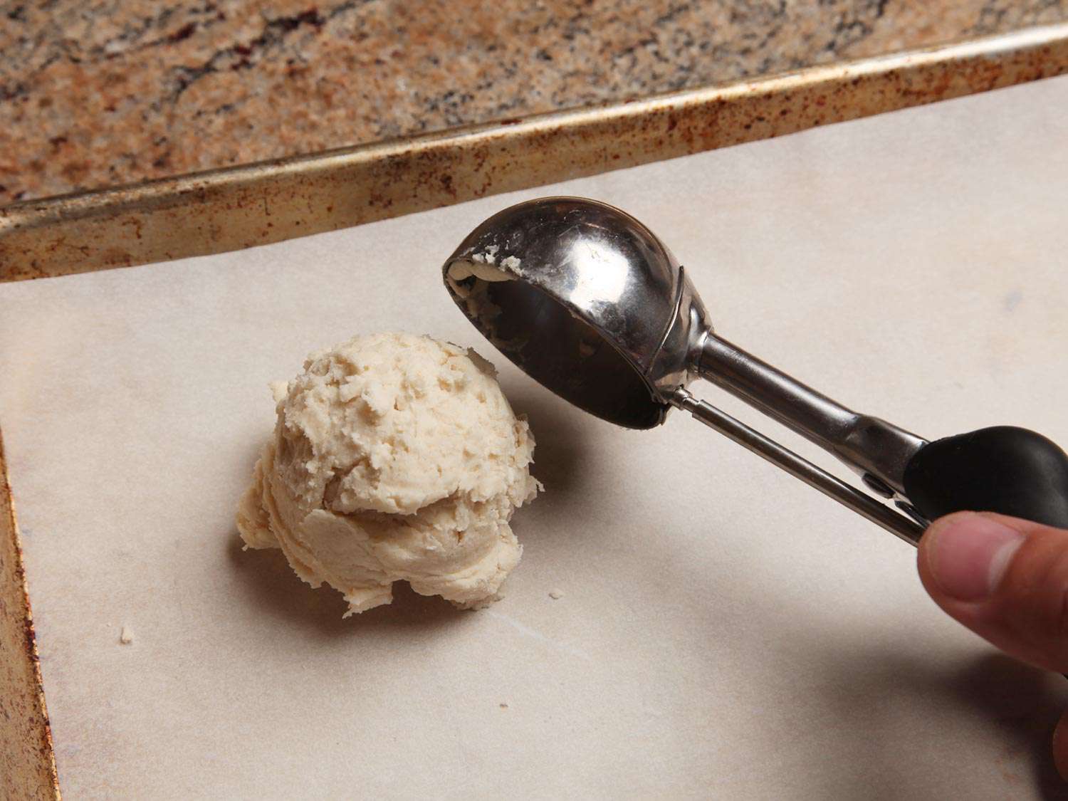 Using an ice cream scoop to scoop biscuit dough onto a baking sheet.