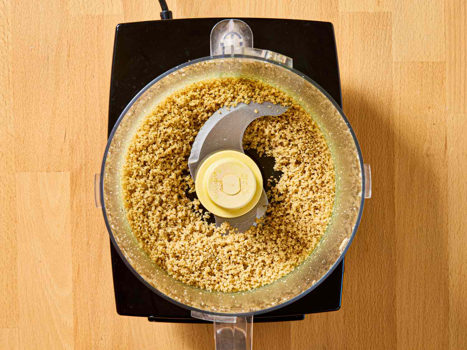 Food processor with ground mixture inside, wooden surface beneath