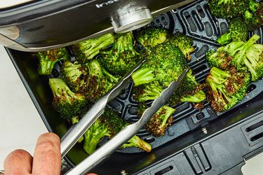 Broccoli being cooked in an air fryer with tongs