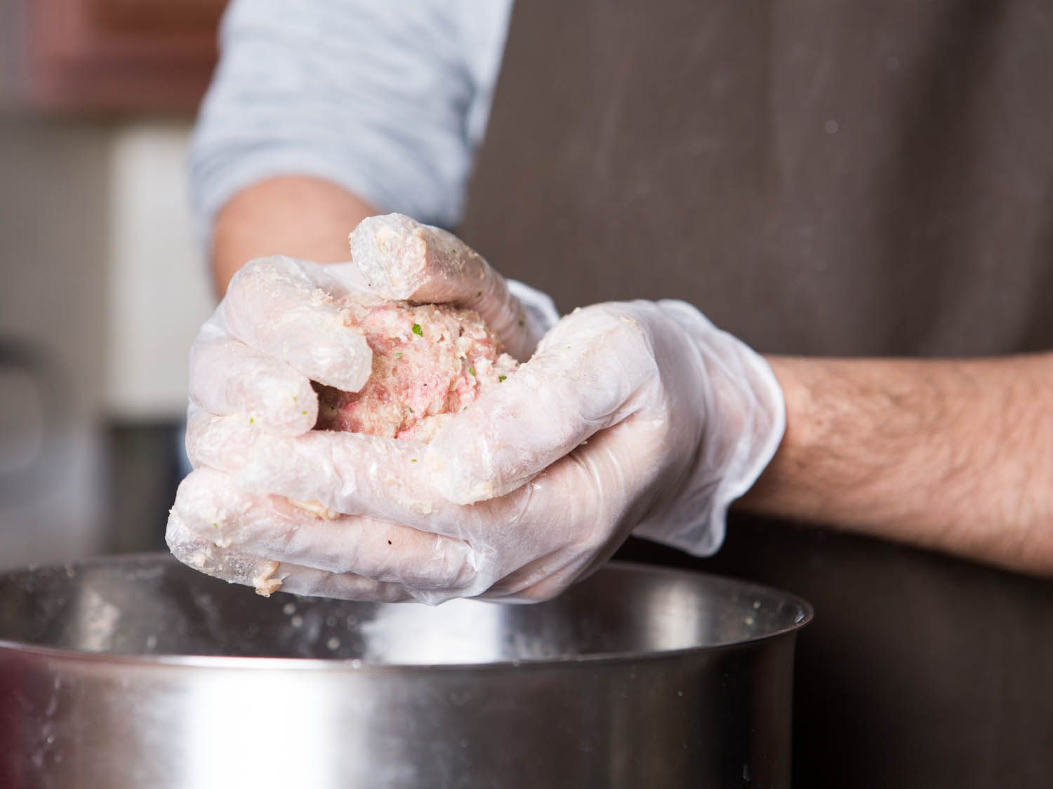Using gloved hands to roll and shape meatballs.