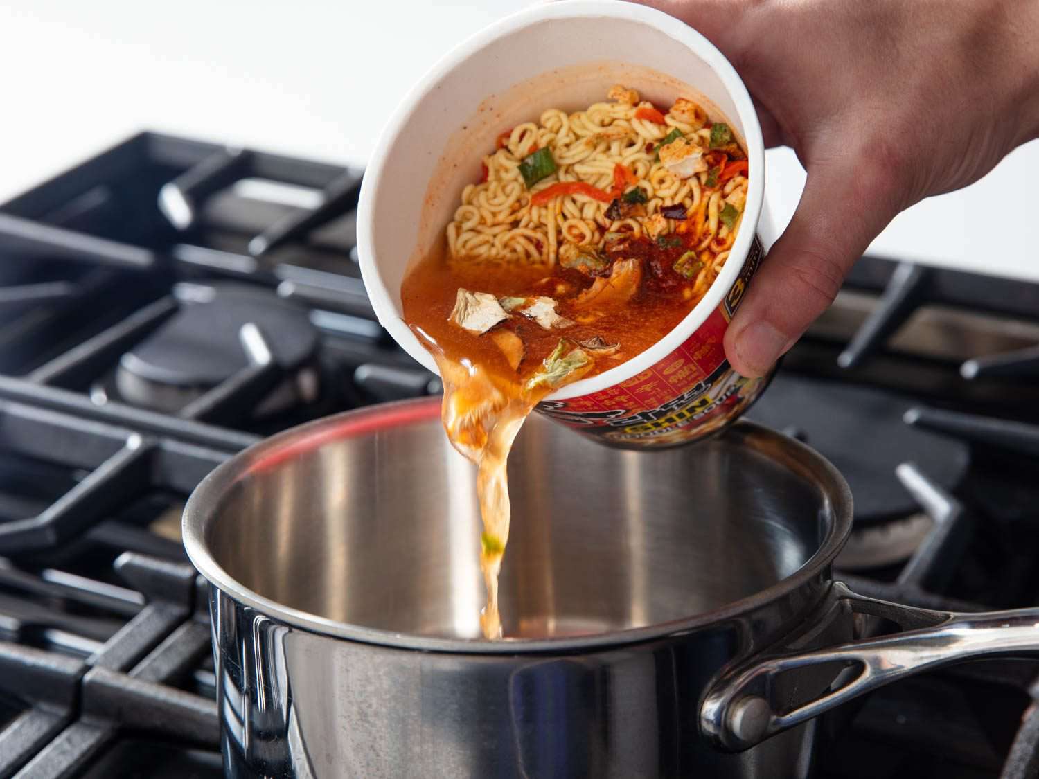 Photo of water poured into Shin Ramyun Cup Noodle being poured into pot on stove for testing