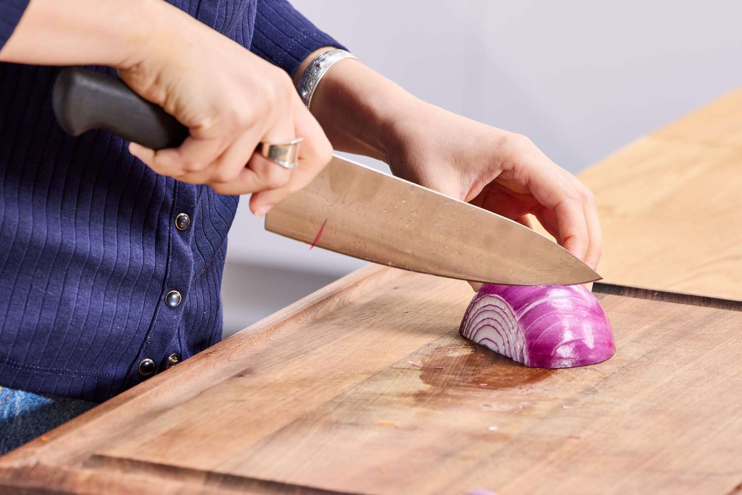 A person cuts into a red onion with the Mercer Culinary 8-Inch Genesis Chef's Knife