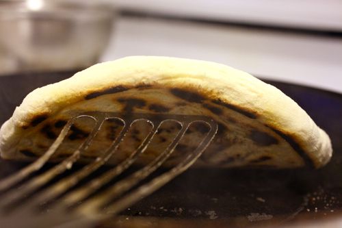 Lifting a Neapolitan-style pizza up from a skillet with a metal spatula. 