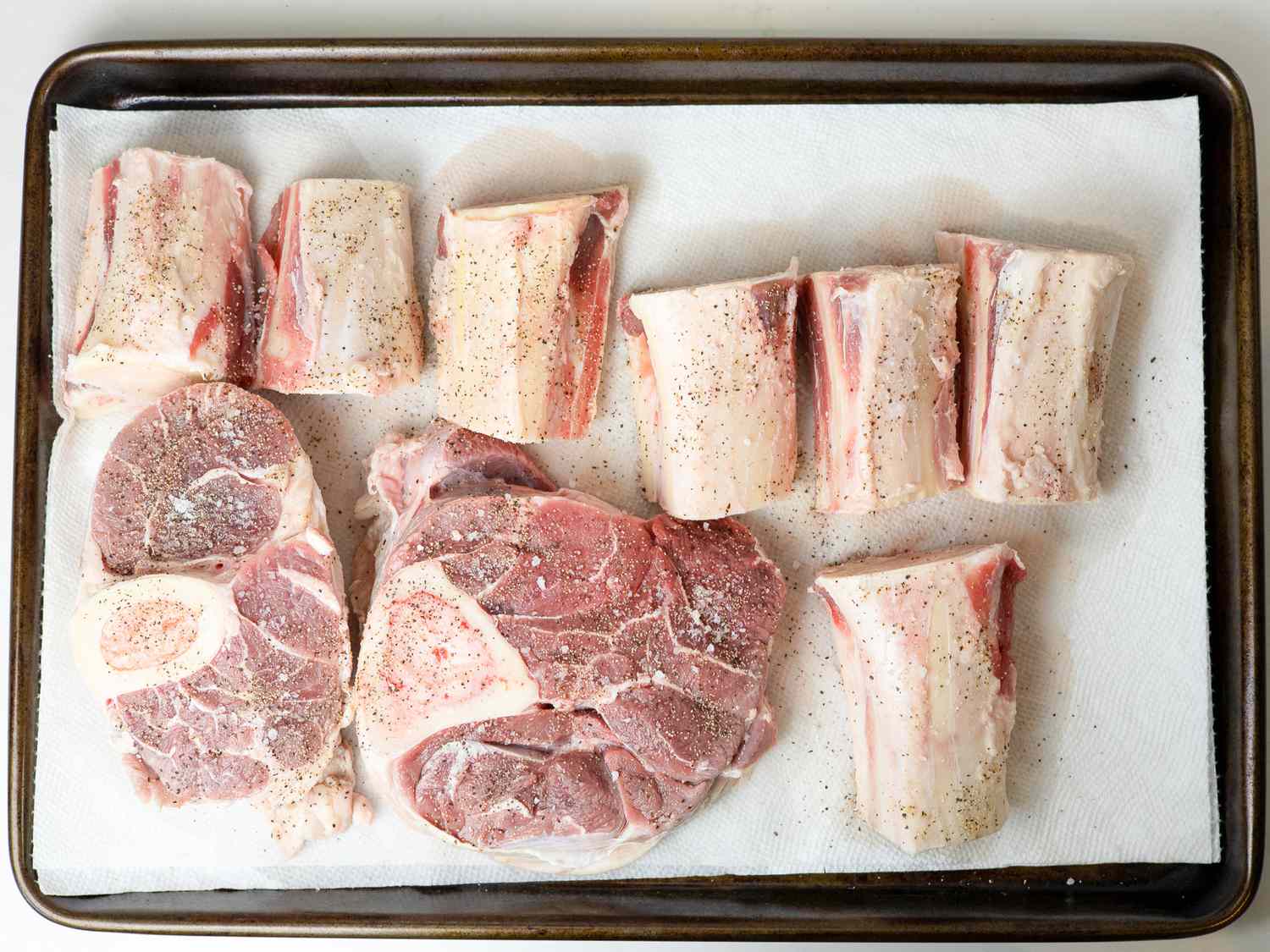 Rinsed marrow bones and beef shanks set on a paper-toweled lined rimmed baking sheet