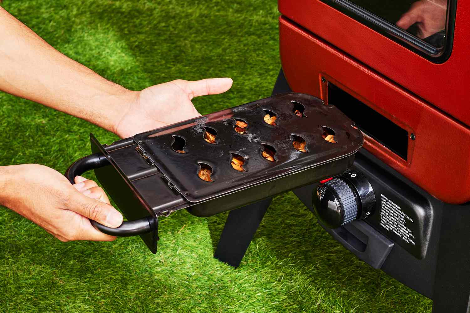 A person adding wood to the fuel chamber of the Pit Boss Vertical Propane Smoker