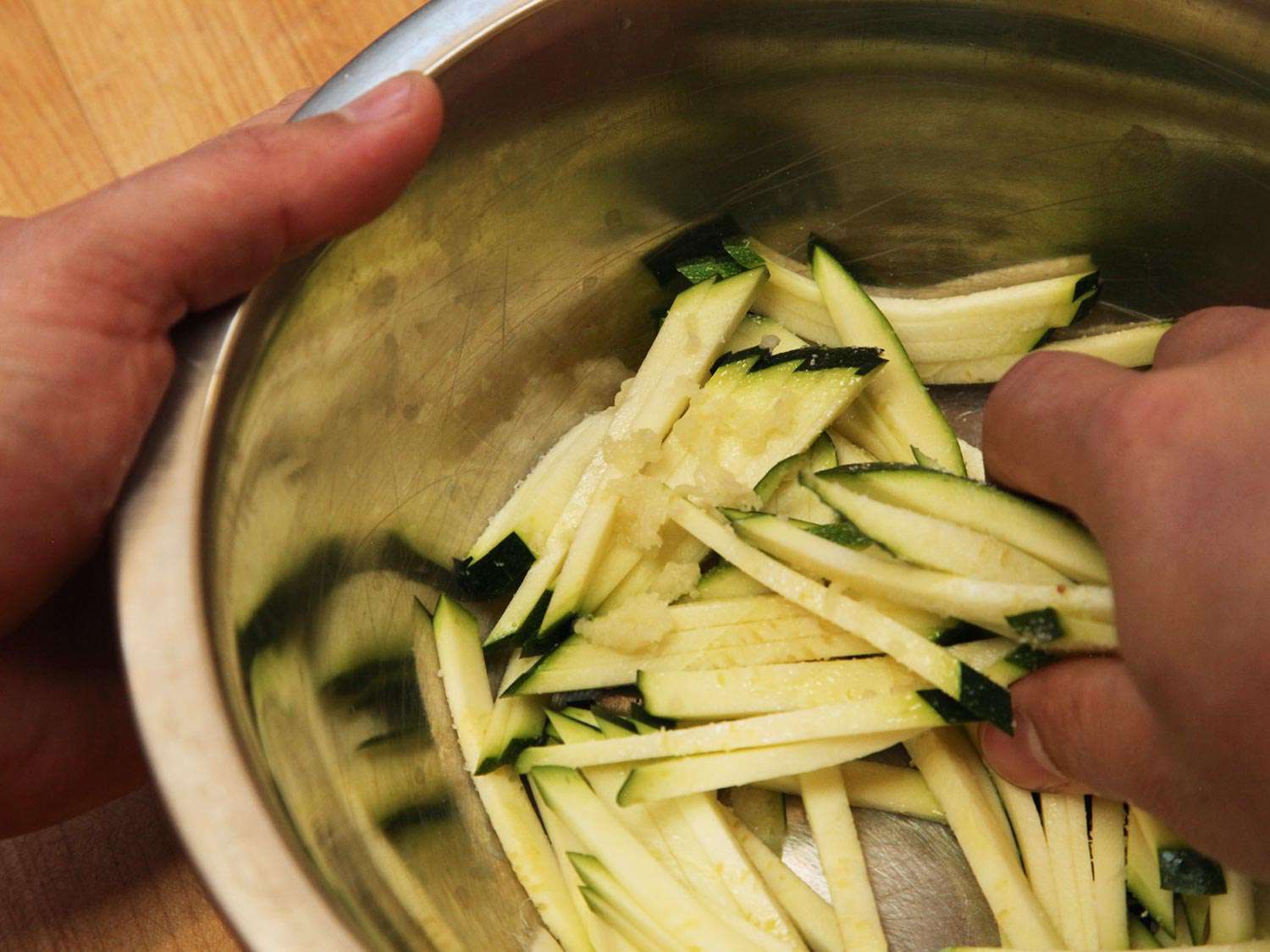 Clsoeup of zucchini matchsticks being tossed with salt in a mixing bowl.