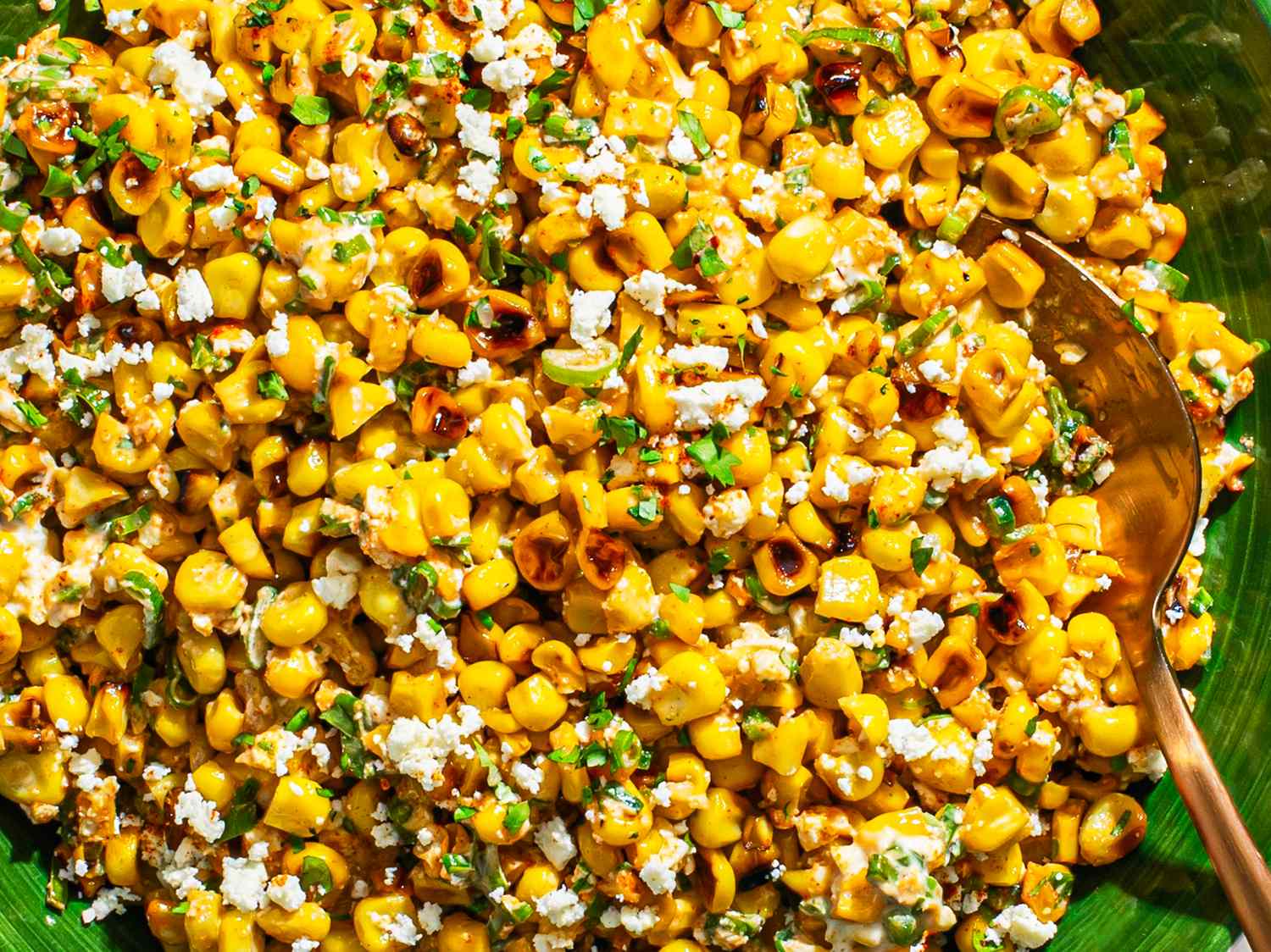 Esquites Mexican street corn salad with cheese and garnish, served in a green dish with a spoon