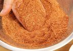 A hand lifting some dry bbq rub out of a metal mixing bowl.