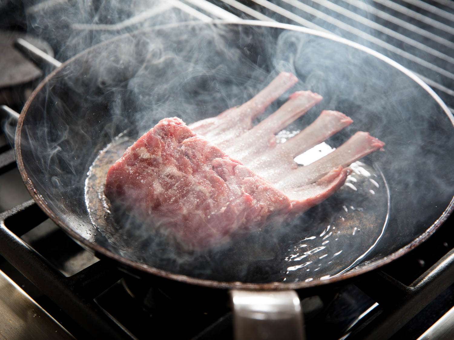 Searing a rack of lamb in smoking hot oil in a skillet. 