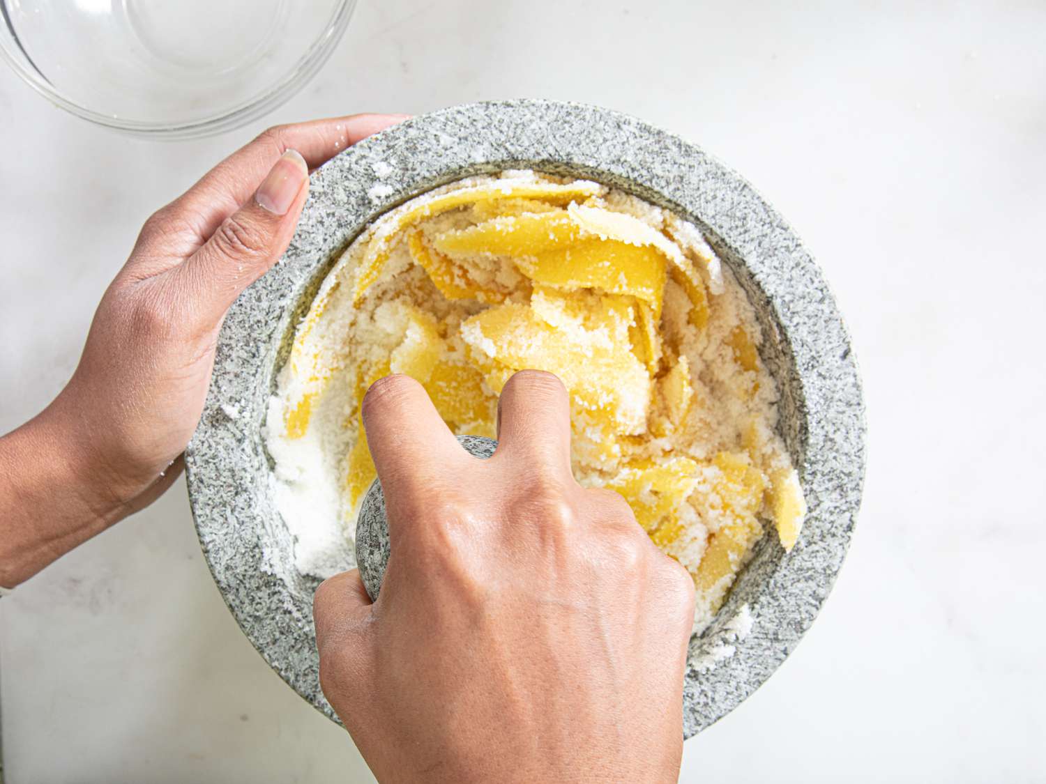 Muddling lemon peels with sugar in a mortar and pestle.