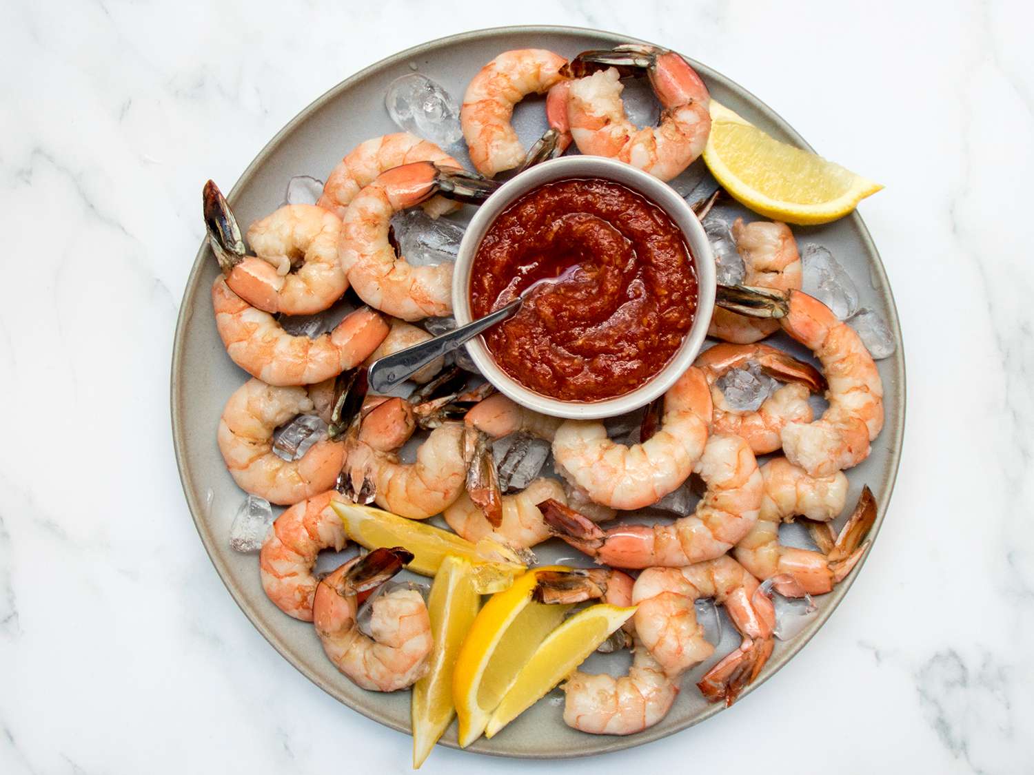 Cocktail shrimp with lemon and cocktail sauce on a plate with ice, on a stone background.