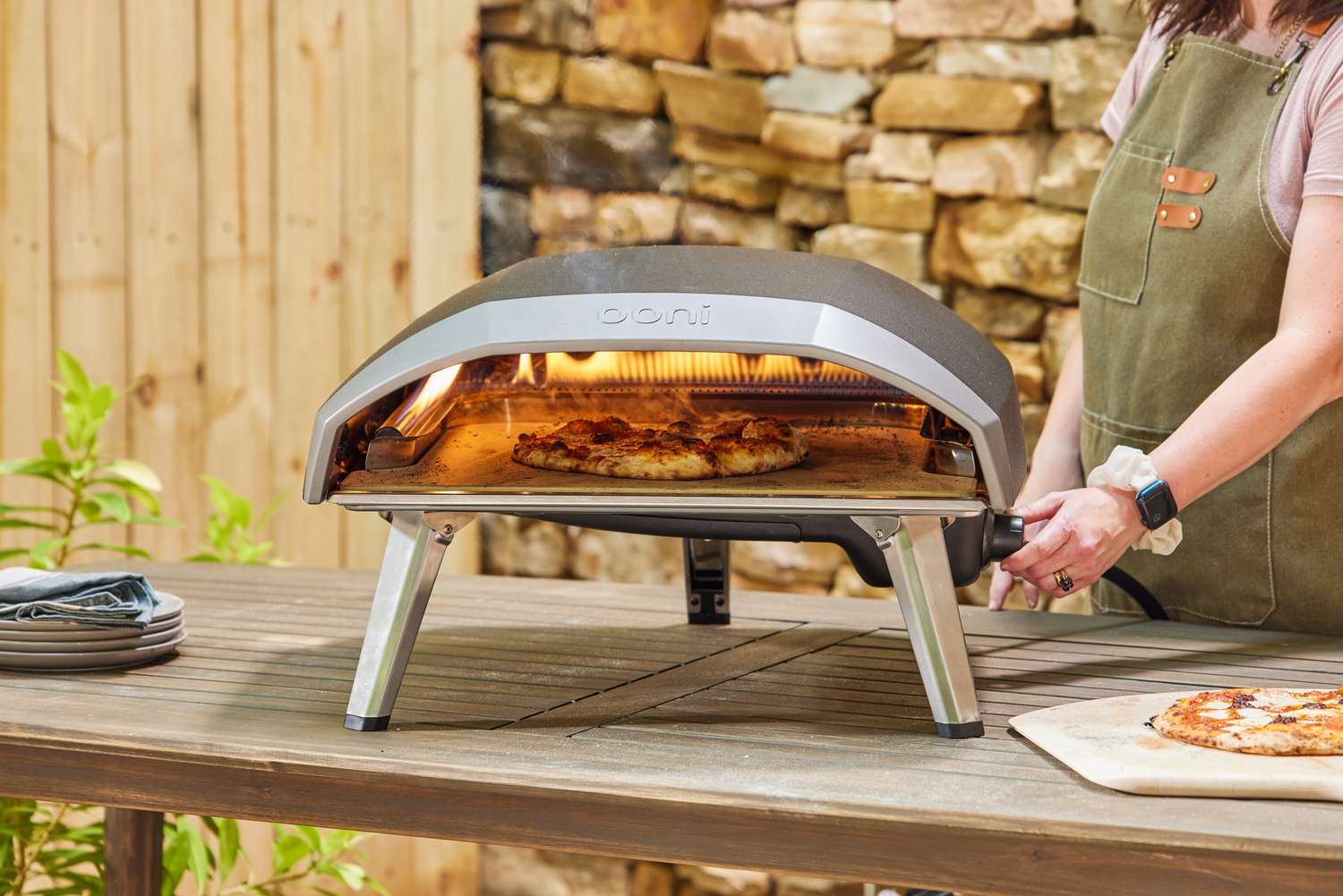 A person turning a nob on the Ooni Koda 16 Gas Pizza Oven while it cooks a pie