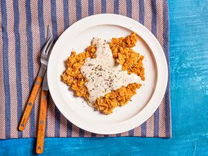 Chicken fried steak on a white plate on a purple and pink stripped towel on a blue backdrop