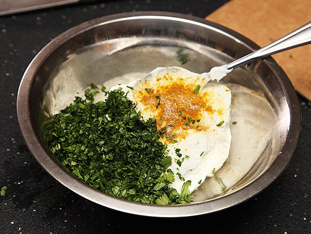 Closeup of a small mixing bowl containing sour cream, chopped cilantro, curry powder, and (presumably) salt.