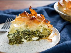 A wedge of spanakopita on a speckled white plate with a fork. 