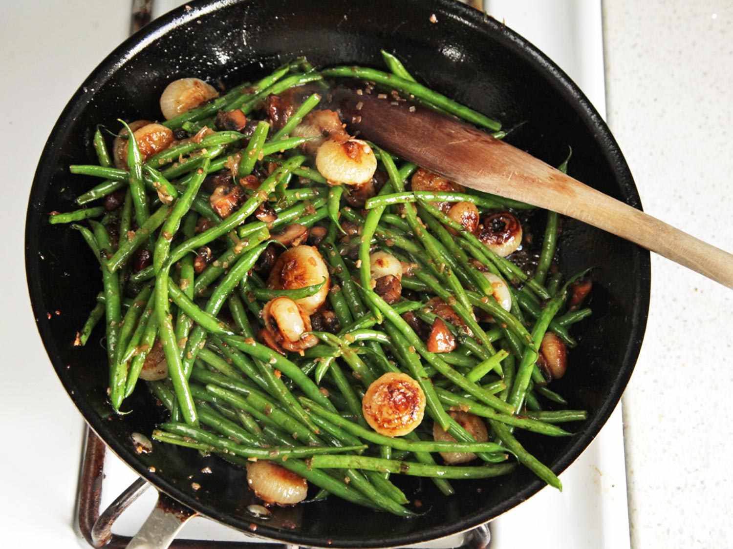 Caramelized onions and blanched green beans are added to the saucepan containing caramelized mushrooms. 