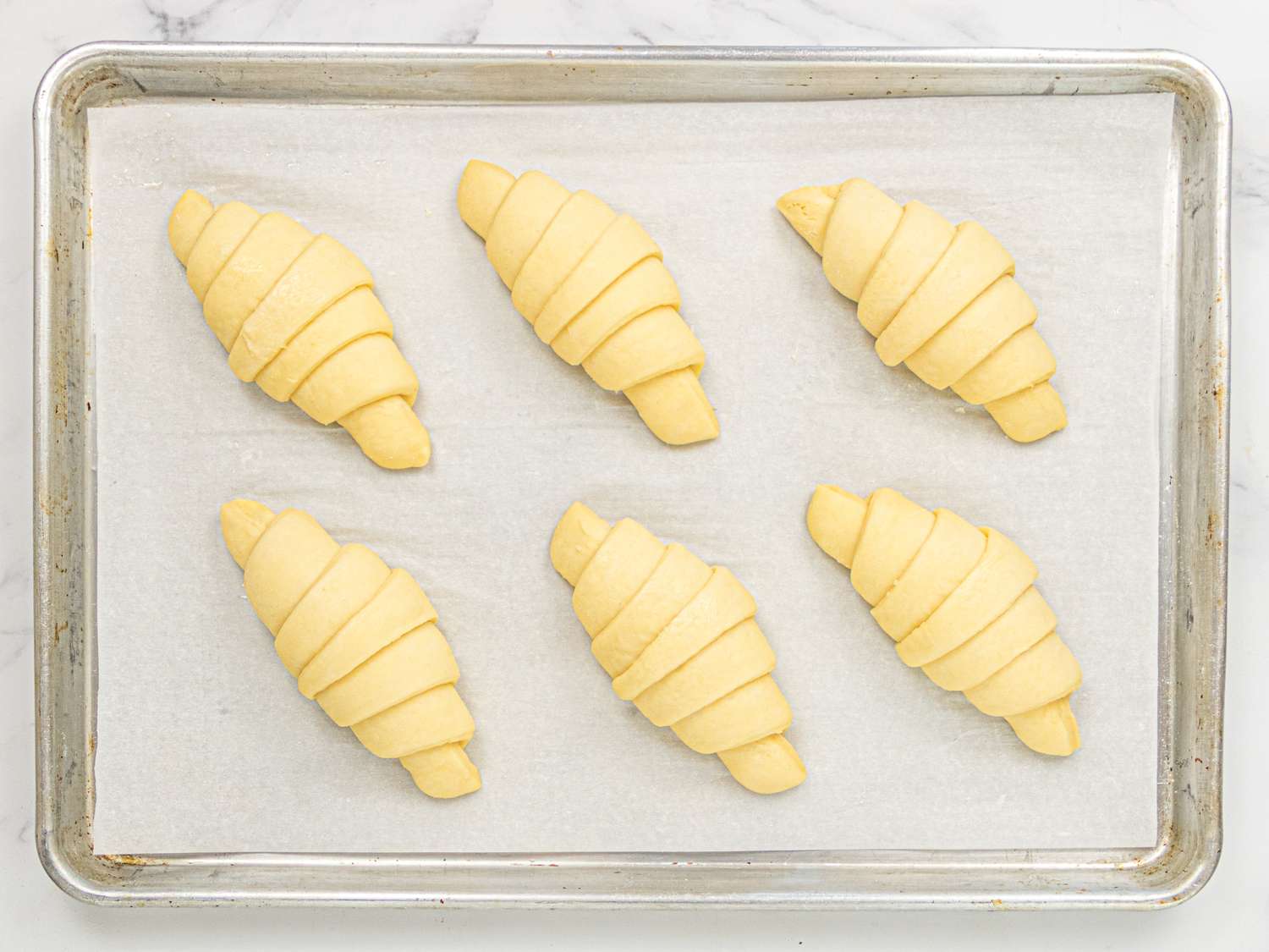 Six unbaked croissants arranged on a baking tray lined with parchment paper