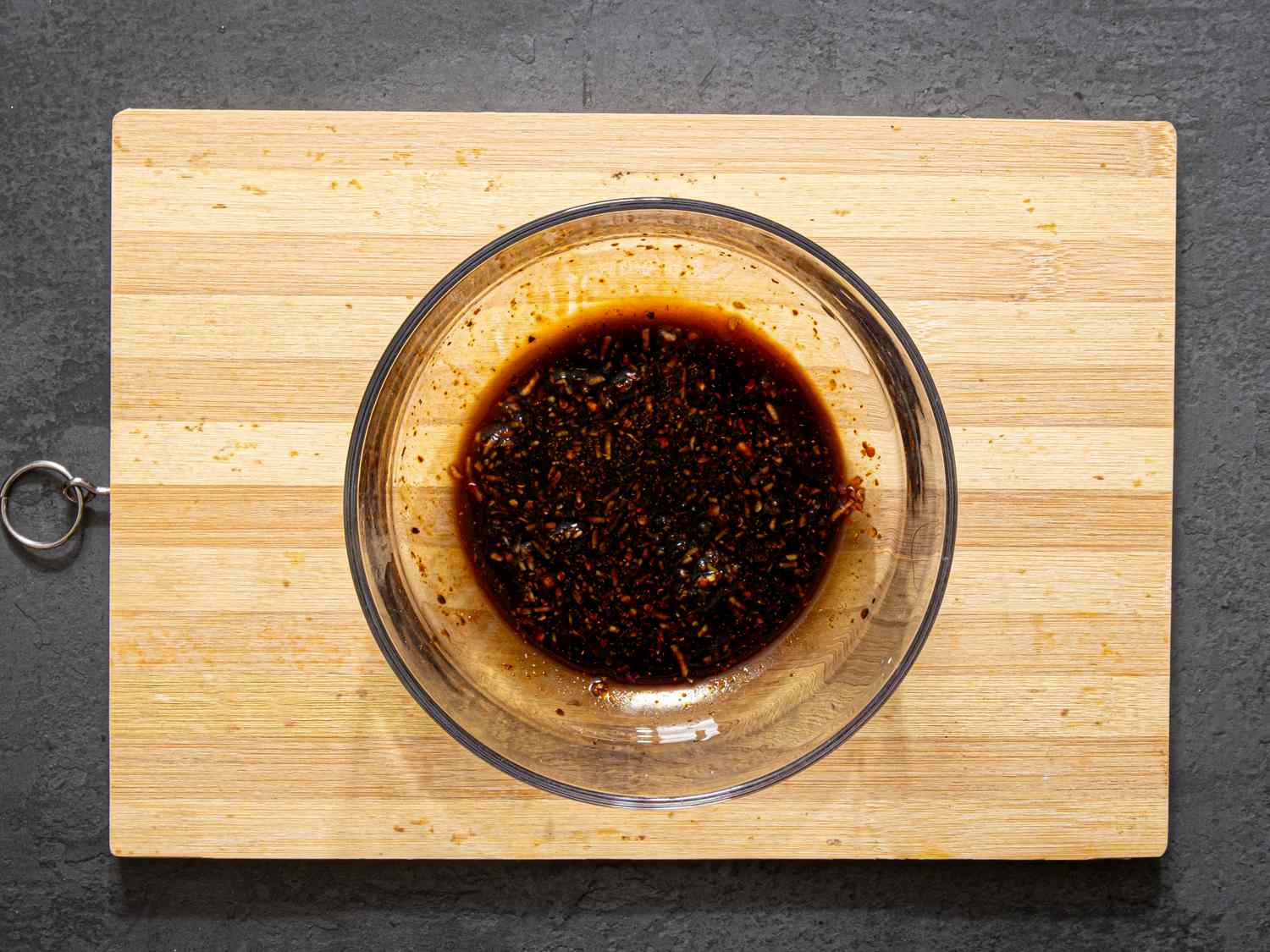 Glass bowl containing dark marinated tofu sauce on a wooden cutting board