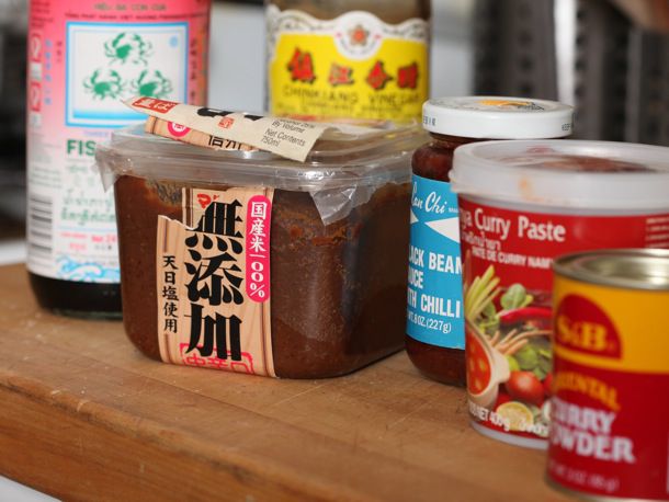 A collection of ingredients to help boost the flavor of ramen on the table, including miso, Japanese and Thai curry paste, black bean sauce. A bottle of fish sauce and Chinkiang vinegar are in the background. 