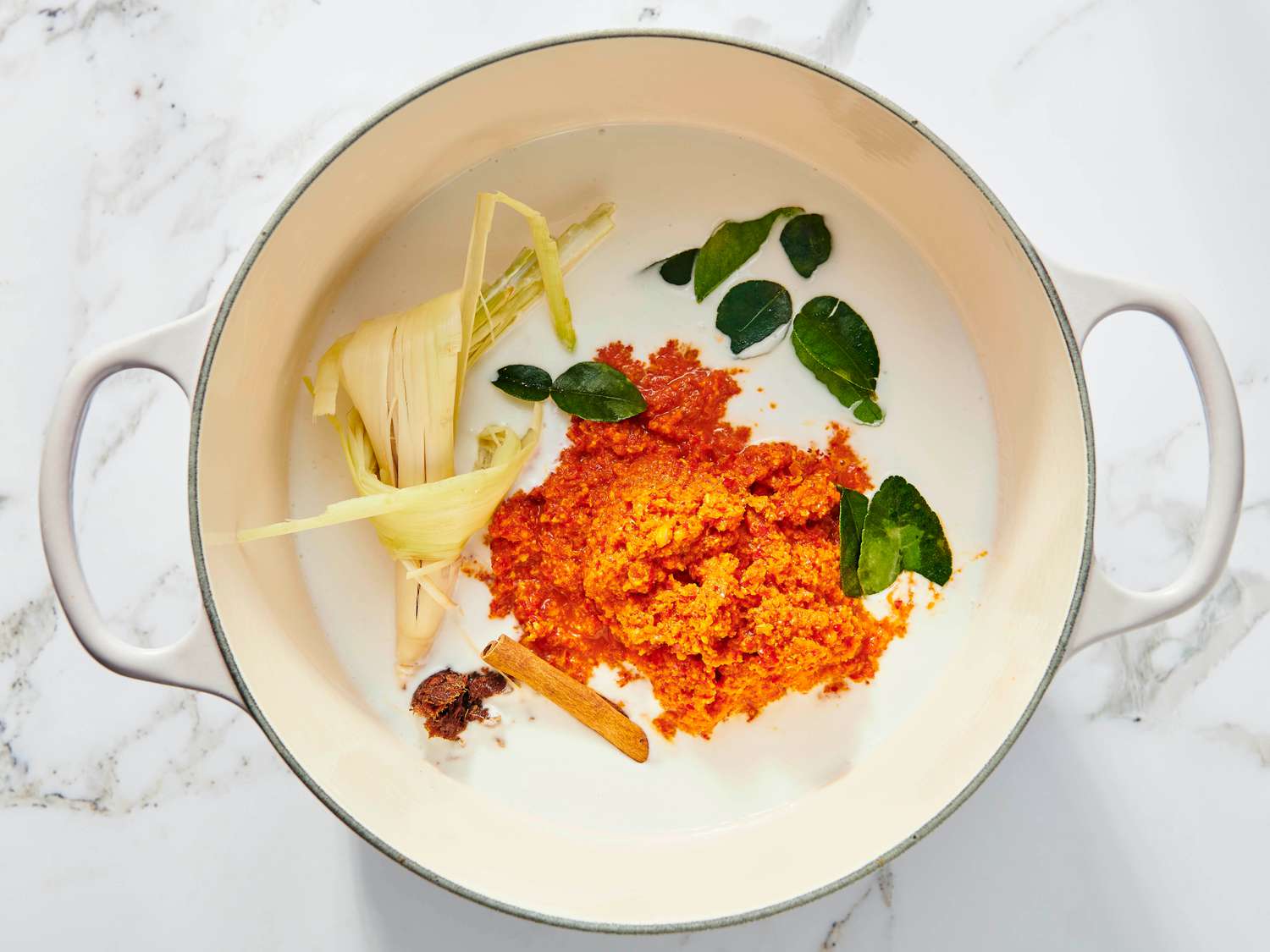 Beef in a dutch oven wirh spice paste, coconut milk, lime leaves, lemongrass, tamarind and a cinnamon stick 