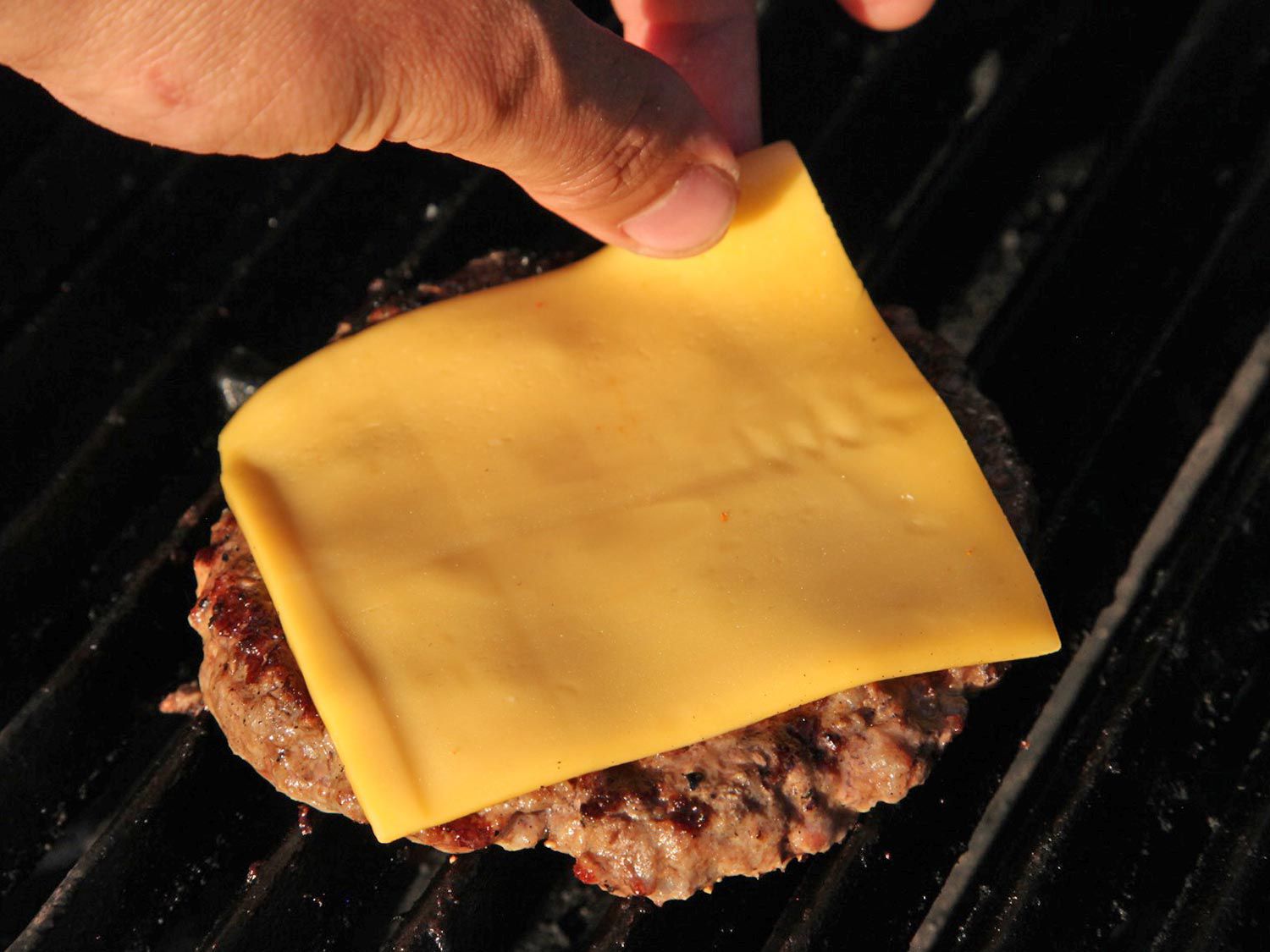 A slice of American cheese is placed on a grilling burger patty.