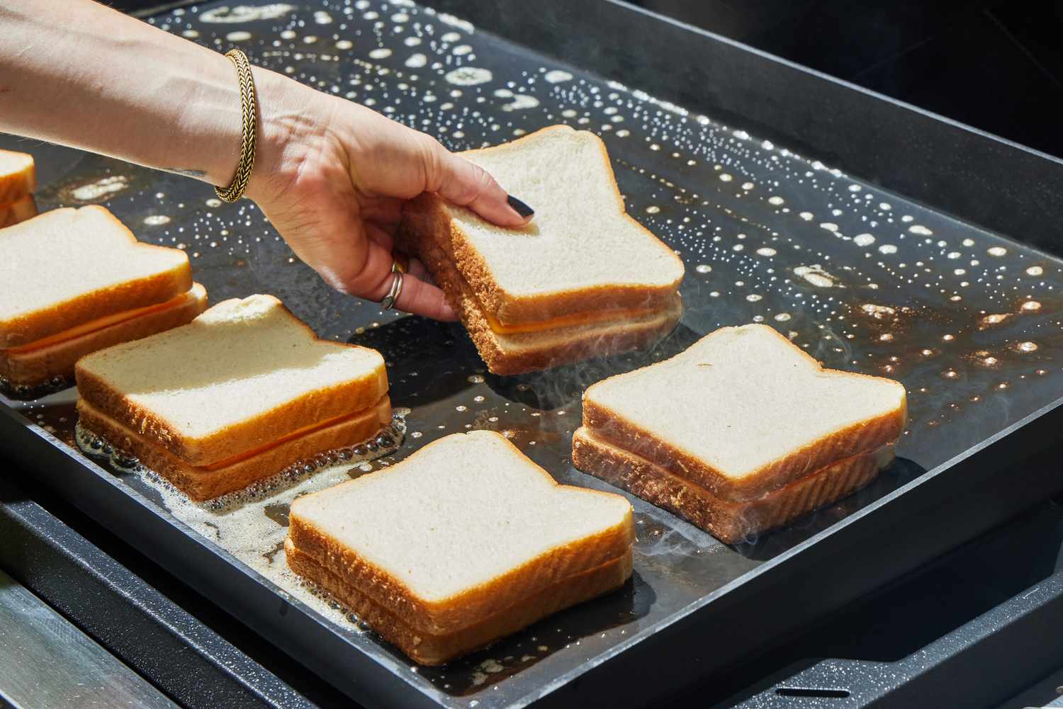 A person cooks grilled cheese sandwiches on the Weber Slate 30 Inch Griddle