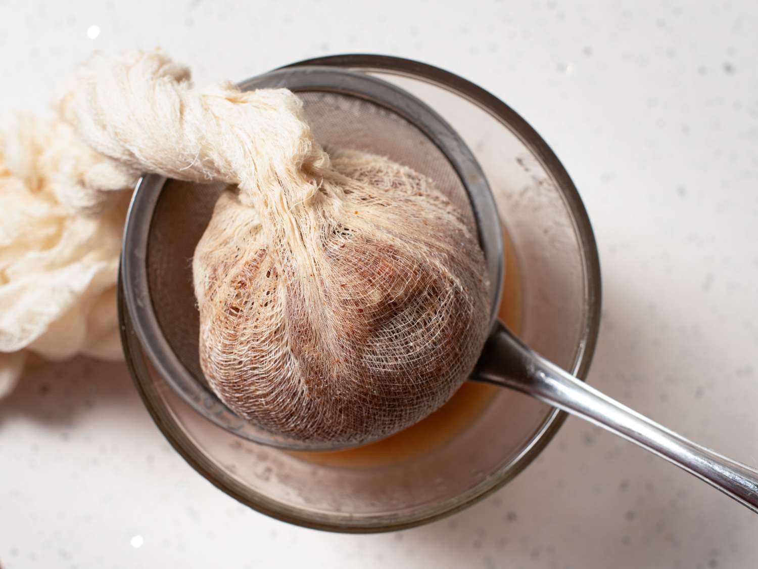 Orgeat mixture wrapped in cheesecloth and strained into bowl.