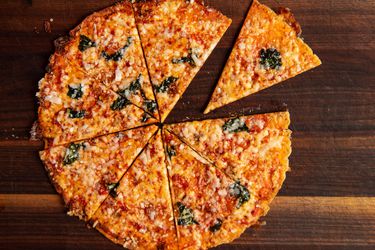 Overhead view of an extra-crispy bar-style pizza, sliced on a dark cutting board.