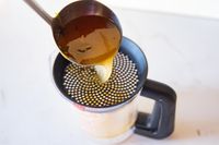 Ladle pouring liquid into a measuring cup with a strainer on top