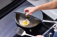 a person opening the williams sonoma splatter screen over a skillet with fried eggs