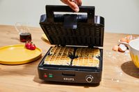 A Krups waffle maker containing 4 cooked waffles