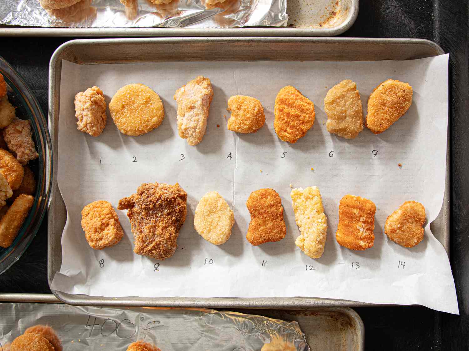 Several chicken nuggets arranged in rows on a baking sheet numbered individually from 1 to 14 for comparison purposes