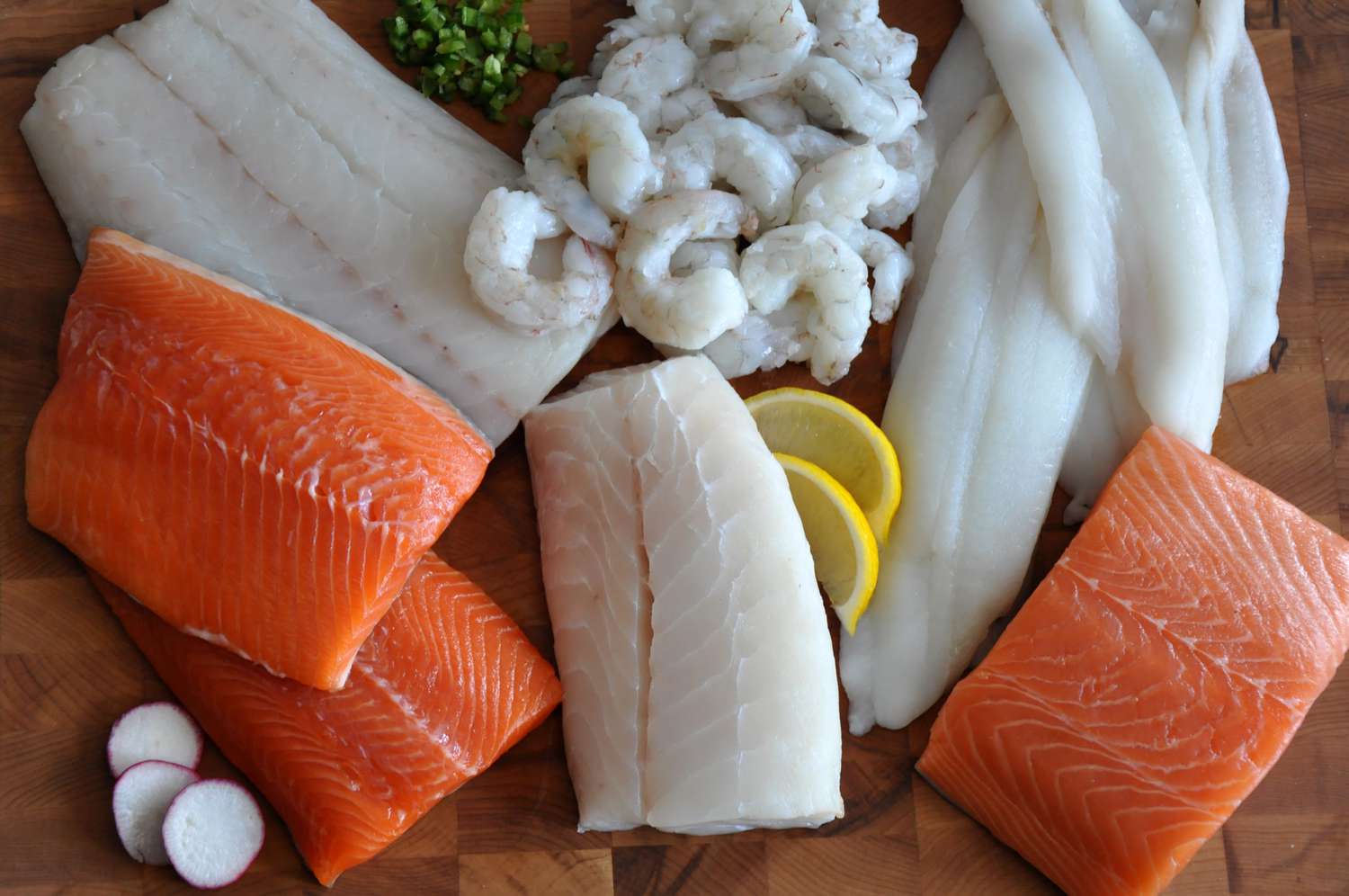 several fish fillets and shrimp on a wooden surface