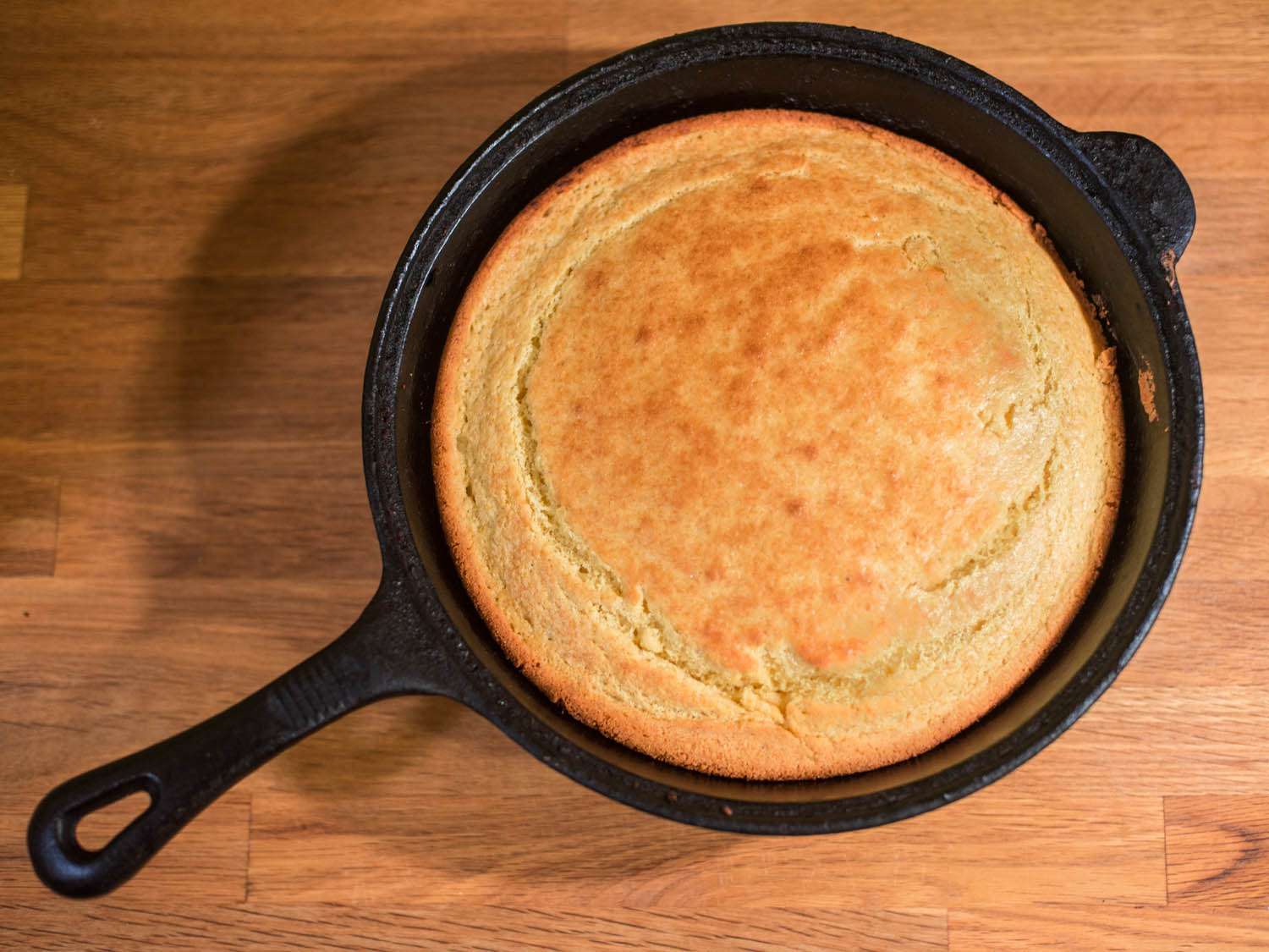 An overhead view of perfectly golden brown cornbread in a cast iron skillet.