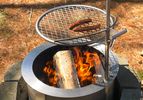 Hot dogs cooking on a grill over a flaming outdoor firepit