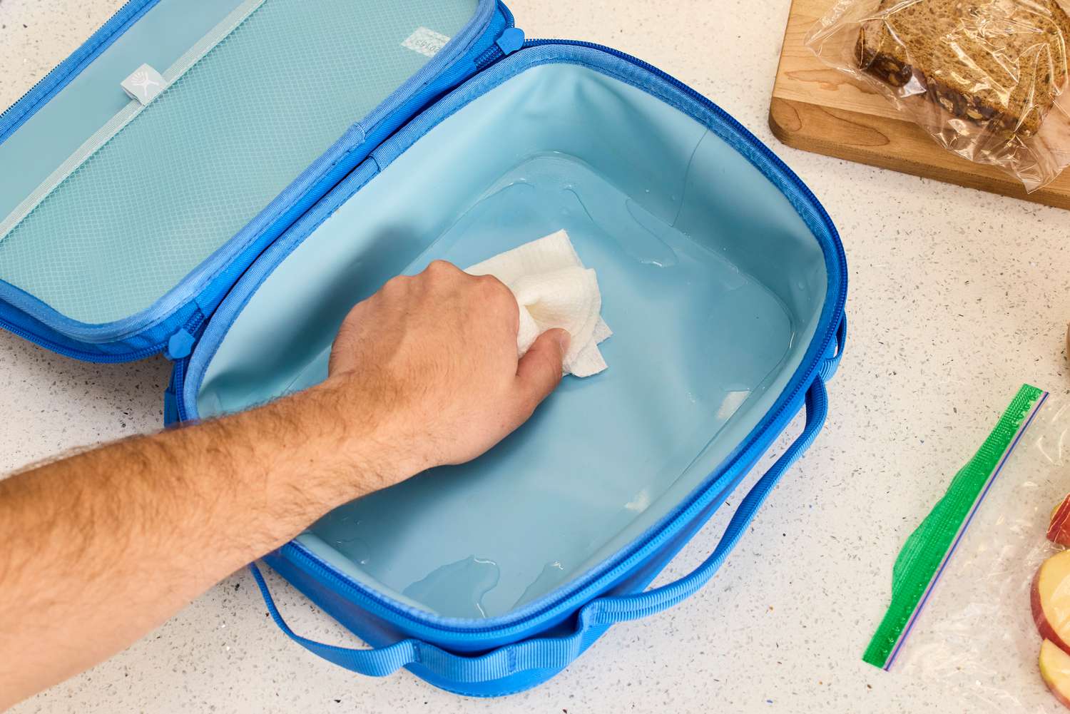 An empty lunch box being wiped clean with water and a paper towel.