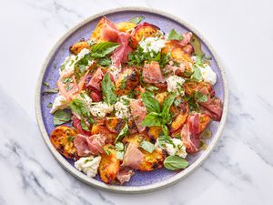 A plate of grilled peach salad with herbs, prosciutto, and cheese