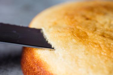 Closeup of a cake layer being sliced along the top edge with a serrated knife.
