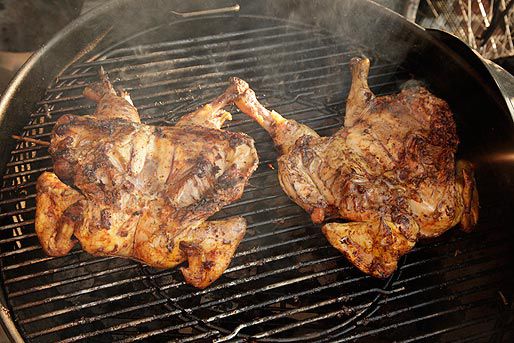 Two butterflied chickens on the grill, breast-side facing down. Their backs are nicely browned.