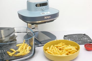 A Ninja Crispi Pro air fryer with cooked crinklecut fries in a glass container and a yellow bowl