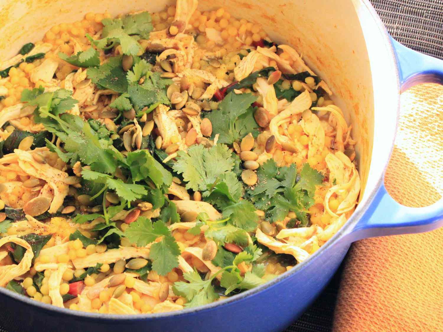 A Dutch oven filled with curried chicken and Israeli couscous topped with fresh parsley.