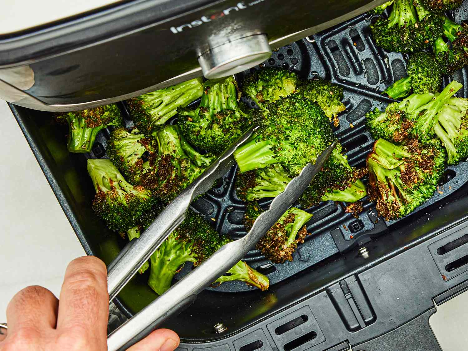 Broccoli being cooked in an air fryer with tongs