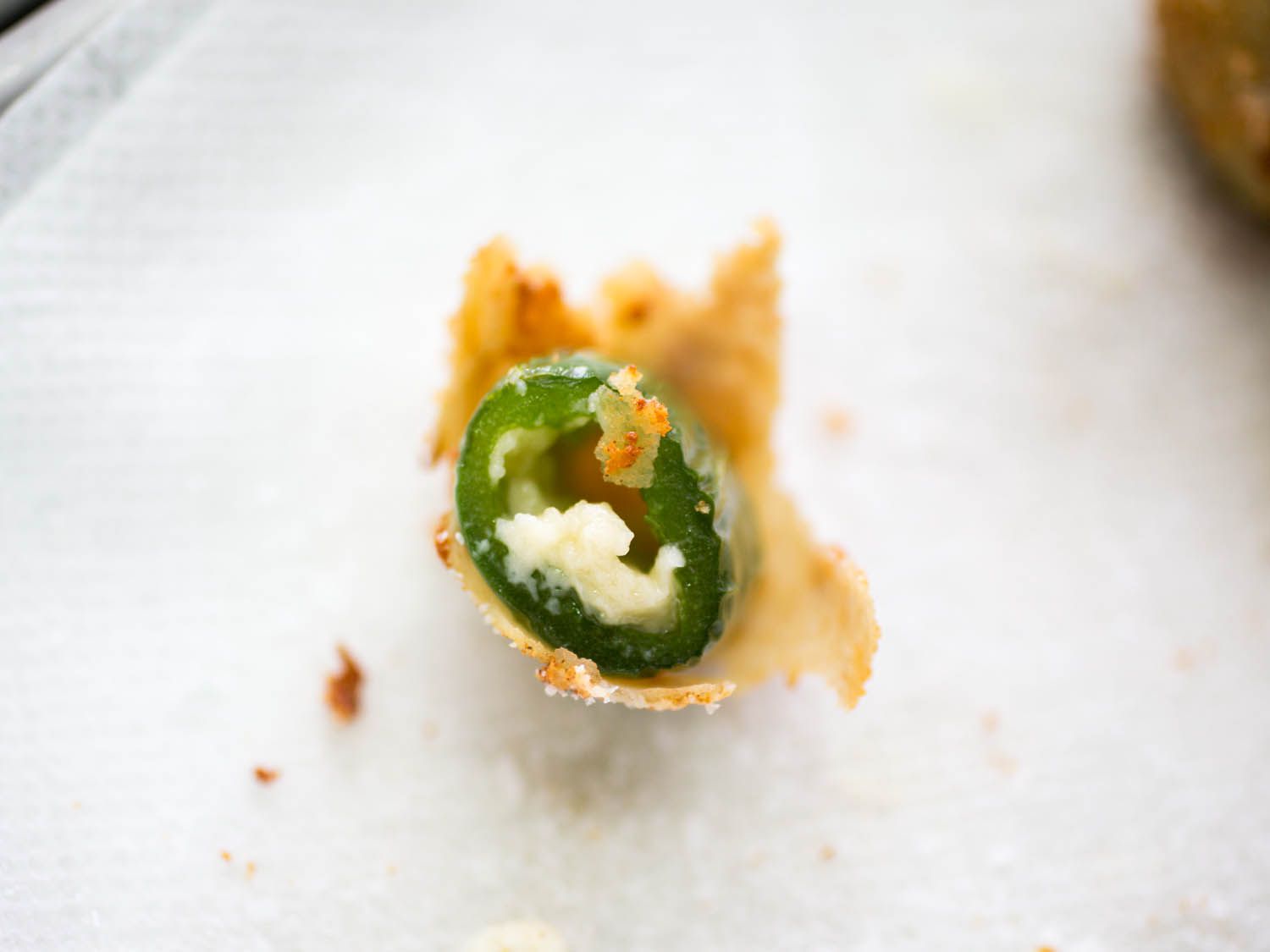 Close-up of a fried jalapeño popper filled with melty American style cheddar cheese. The breadcrumb coating has ruptured and most of the cheese has leaked into the fry oil.