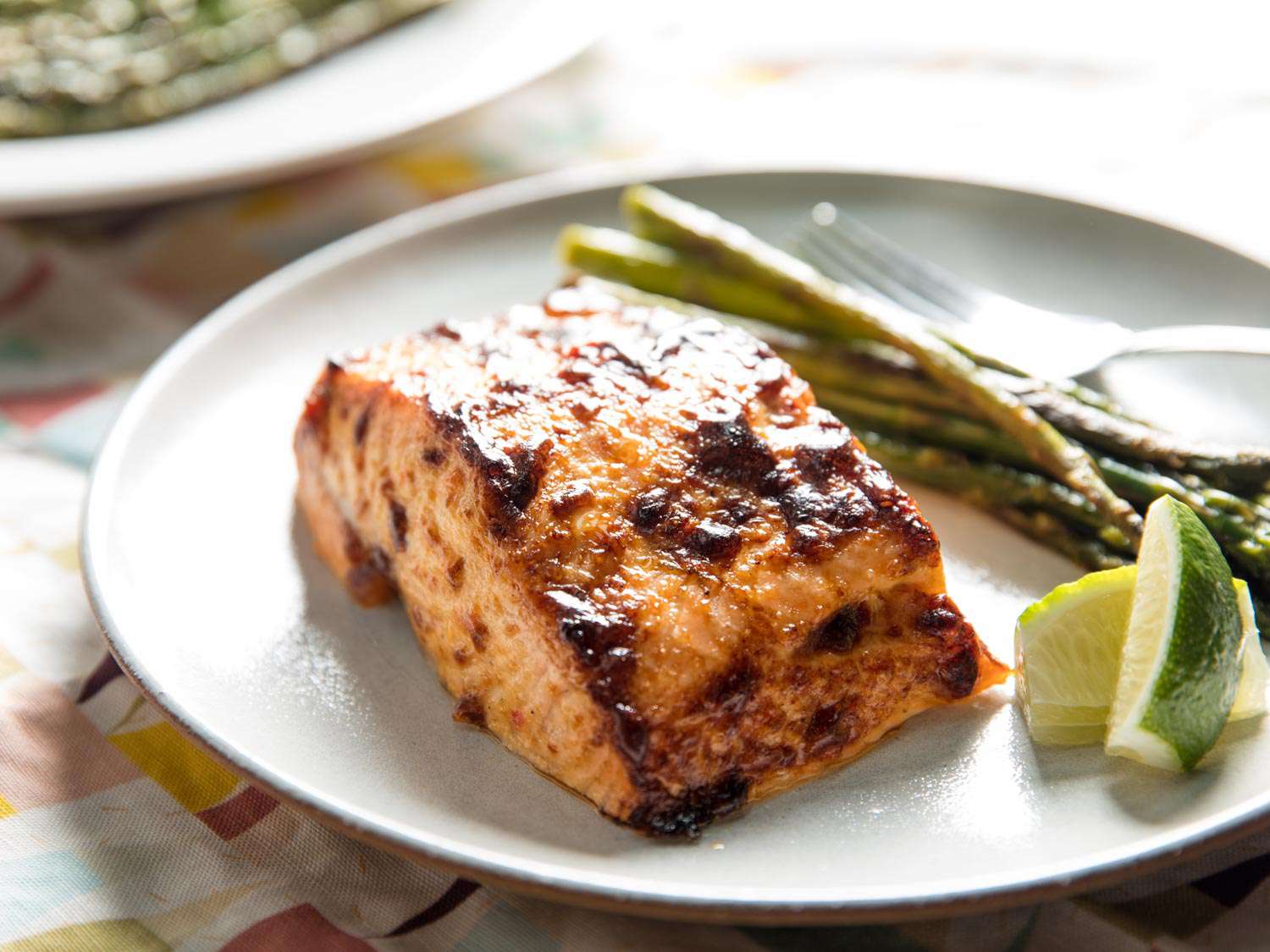 A serving of the finished broiled salmon, served on a white plate with lime and asparagus.